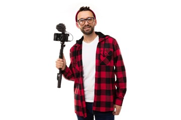 a young blogger on a white background in a plaid shirt and glasses for vision holds a camera with a...