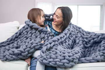 Mother and daughter wrapped in blanket on white couch