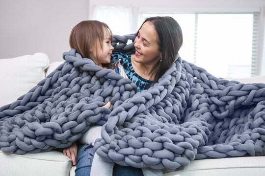 Mother And Daughter Wrapped In Blanket On White Couch