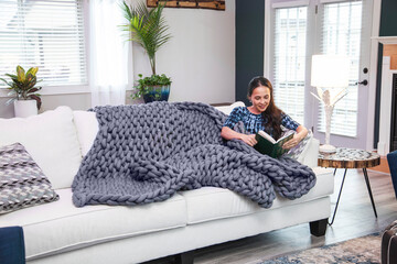 Woman reads on white couch with weighted blanket