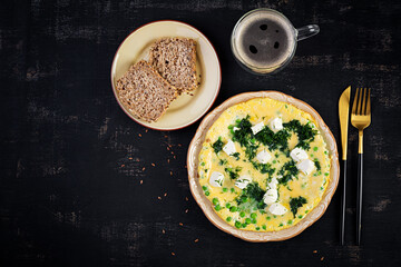 Healthy breakfast. Omelet with green peas, feta cheese and dill. Dark background. Top view
