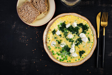 Healthy breakfast. Omelet with green peas, feta cheese and dill. Dark background. Top view