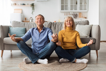 Senior Spouses Meditating With Eyes Closed Doing Yoga At Home