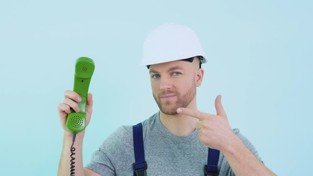 Serviceman in overalls and helmet holds an old phone in his hands and points to it