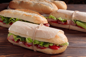 Close-up view of three banh mi sandwich with sliced grilled pork and peppers and salad packed in paper on wooden background. Selective focus.