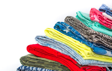 A stack of multi-colored clothing and various jeans neatly folded on a white background. Rainbow fabrics for sewing, close-up. Fashion and style, casual wear.