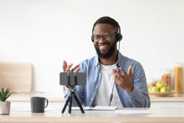 Friendly glad young african american bearded guy teacher in glasses and headphones shooting video...