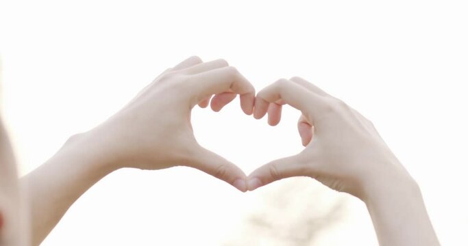 Make heart shape with hand through sunlight. Symbol of love and take care and cherish.