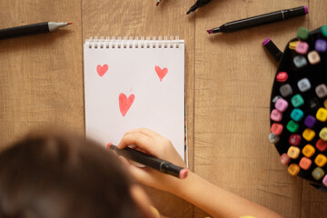 child girl draws sketch with markers. drawing of hearts.
