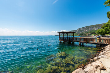 Lake Garda in front of the small Garda town. Beautiful bay with a wooden pier with roof and the...