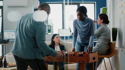 African american woman playing at foosball table with man after work at office. Workmates enjoying...