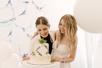 Obraz na płótnie Canvas Two beautiful blonde girls with a cake on a light background
