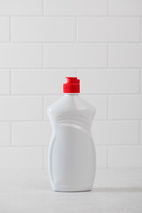 A mockup of a white plastic bottle with liquid dishwashing detergent with a white tiled background.