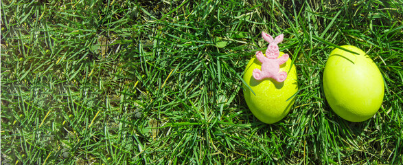 A rabbit toy and two decorative Easter eggs in the green grass. Top view, copy space and space for text on the left