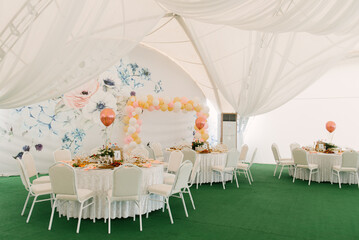 A beautifully decorated party with balloons in a large white tent with a photo zone, catering and a...