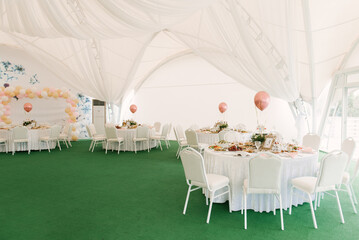 A beautifully decorated party with balloons in a large white tent with a photo zone, catering and a...