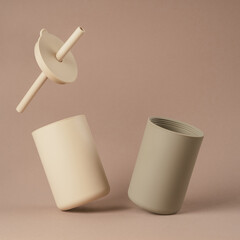 Modern colorful pastel beige and grey silicone sippy glasses with straws standing by side on brown background. Baby tableware, first feeding, serving concept. Instagram use, square frame, levitation.