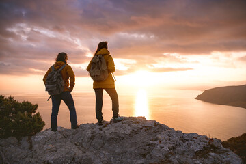 Two hikers with backpacks looks at sea sunset from view point