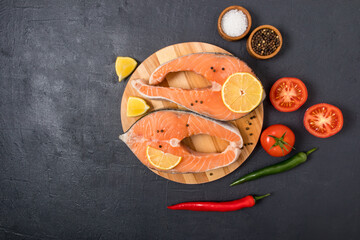 top view of two fresh salmon steaks on a round wooden board with lemon, pepper and tomatoes. the concept of healthy eating, cooking healthy food.