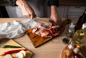 the farmer's hands cut a fresh piece of meat on a wooden board on the countertop. ingredients for cooking at home. proper nutrition.