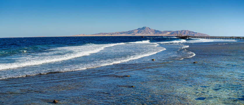 Sea landscape on the Red Sea with silhouettes of Tyrant Island on skyline, Egypt. Panorama of  the coast line with sea waves on the coral reef at storm near the Nabq bay, Sharm el-Sheikh, Sinai.