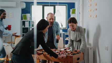 Happy woman winning game at foosball table do to fun activity at office after work. Workmates...