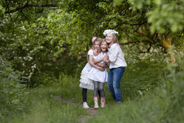 Three teenage girls in white blouses are laughing and playing, friendly hugging.  Children's fun in nature in summer, holidays, happy childhood concept