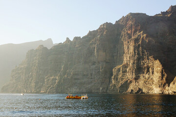 Boat on the sea by dramatic vertical cliffs called Acantilados de los Gigantes, located on the coast of Tenerife, Canary Islands