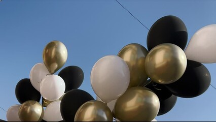 White, black and golden balloons filled with helium moving with the wind against bright blue sky