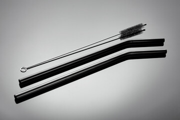 A small brush and reusable straws for drinks on a gray glossy background. Ecology protection concept
