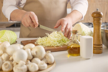 man prepares  hodgepodge of cabbage and mushrooms in  kitchen at home