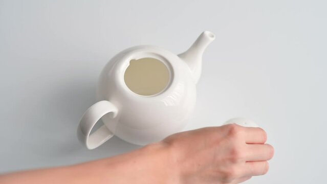 Dry tea leaves are pouring from spoon into white ceramic teapot on white table. Concept of brewing tea. Classical tea ceremony. Green, black, herbal tea in a teapot. Healthy Lifestyle