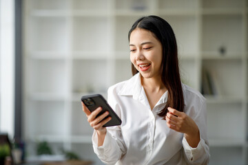 Portrait of a happy Asian businesswoman using mobile phone indoor, Asian businesswoman working in modern office.
