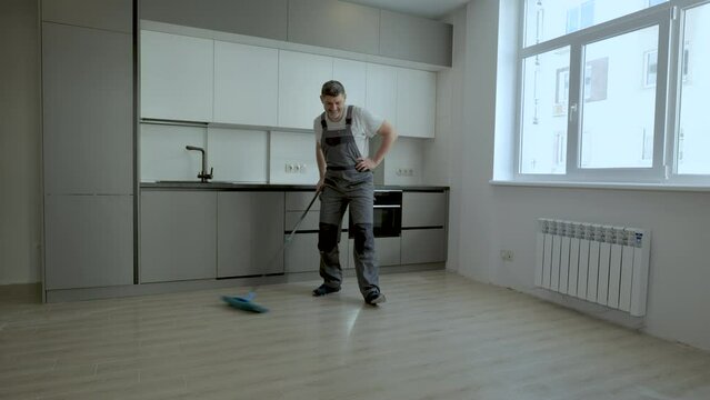 A Cheerful worker in uniform washes the floor in a new apartment