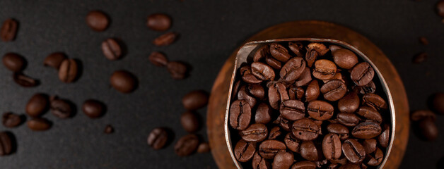 Fragment of a crucible filled with coffee beans, black tabletop with scattered coffee beans in the background.