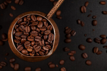 Crucible filled with coffee beans standing on black countertop with scattered coffee beans, top view.