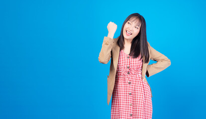 Excited business asian woman holding fist arms hand smile happiness success job or lucky standing over isolated blue background. Positive girl raised arms hand for new job. Lifestyle, winner concept.