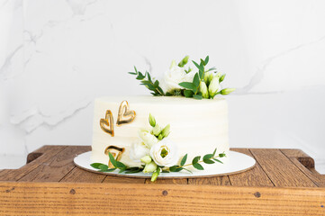 Sweet cake with floral decor on wooden stand over marble wall. Wedding cake