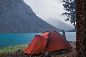 red tent on the shore of a mountain lake on a rainy evening
