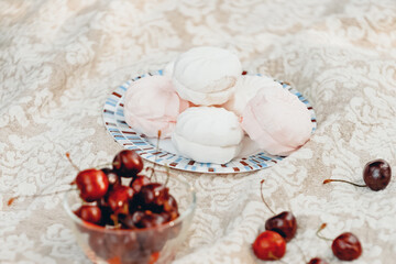 Fototapeta na wymiar plate with marshmallow and glass bowl with cherries on white tablecloth. Vintage still life. Selective focus