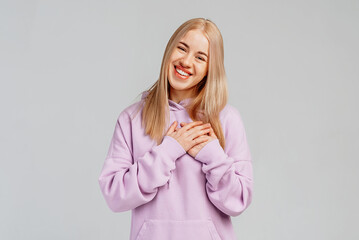 Happy young woman makes gratitude gesture presses palms to heart feels touched pleased by...