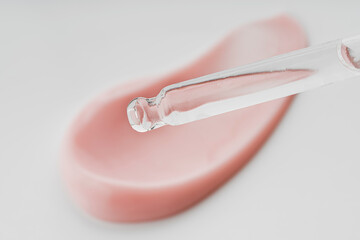 Cosmetic pipette with drops of oil, on the background of cosmetic cream smear.