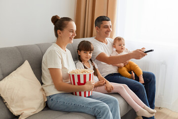 Side view portrait of happy family sitting on couch and watching films with popcorn, expressing positive emotions while watching tv together, enjoying leisure time.
