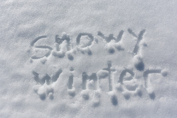 Inscription Snowy winter, written on white surface of the snow.Top view. Flat lay. Winter holiday. Side sunlight.