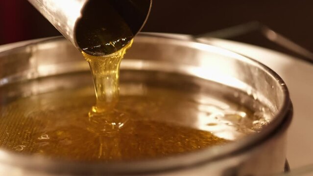 Extreme close up of fresh healthy honey bee poured from metal pipe in a jar. Dense liquid gold nectar from organic apiculture farm