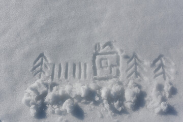 Child's drawing on the white fluffy surface of the snow. The house, Christmas trees, fence and the sun are drawn.