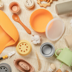 Pastel silicone set of tableware, cutlery, bib, accessories and wooden toys for children on white cloth background decorated with cotton and spica. Baby accessories, tableware concept. Flat lay.