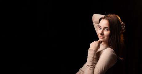 Portrait of a young woman on a dark background. The girl in the brown sweater. Friendly face looking at the camera. Place for text. Banner.