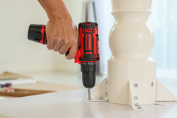 man assembling white table furniture at home using cordless screwdriver