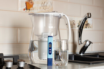 Measurement of TDS of water. Electronic pH meter in a glass of water. Filter for water purification. There is a tap for drinking water in the background. 